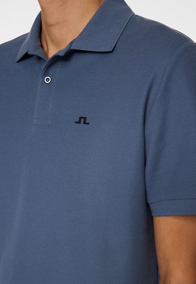 Blauwe polo van textiel met een structuur, voorzien van een kraag, een drukknoopsluiting met drie knopen, en een klein zwart logo op de borst.