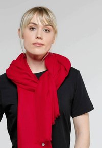 Punane, pehme sall, mis on kaela ümber mähitud ja frantsiotega otstes. Must lühikeste varrukatega T-särk, sileda tekstuuriga ja vabalt istuv.
