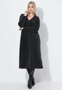 Schwarzes, langärmliges Kleid mit einem V-Ausschnitt, aus einem glitzernden Material, knielang, mit einem lockeren Schnitt und seitlichen Schlitzen.