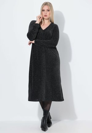 Vestido negro de manga larga con escote en V, hecho de un material brillante, de longitud media, con un corte holgado y detalles de abertura lateral.