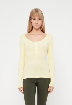 Langärmliges, geripptes Oberteil in hellgelb mit einem U-Boot-Ausschnitt und einer Knopfleiste mit fünf Knöpfen. Fitted-Design ergänzt die grünen Hosen.