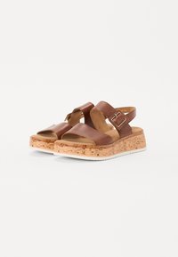 Brown leather sandals featuring a cork wedge sole, open-toe design, dual straps, and a side buckle for adjustment.