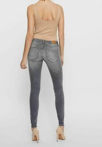 Jeans ajustados grises de mezclilla, con una cintura de altura media, bolsillos traseros y un desgaste sutil. Llevados con una camiseta sin mangas de color beige ajustada.