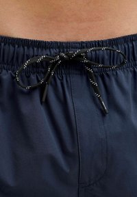 Tengeri kék úszóshort elasztikus derékkal és fekete zsinórral, fehér pöttyökkel. Simaság, könnyű anyag, látható varrással.