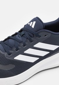 Navy athletic shoe with mesh upper, white three-stripe design, lace-up closure, and textured rubber outsole, marked 'CLOUDFOAM'.