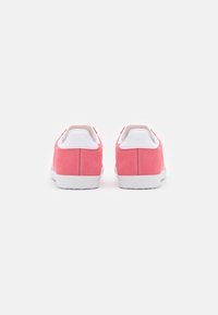 Pink suede sneakers with white rubber soles and accents, featuring a smooth, rounded design and a low-top silhouette.