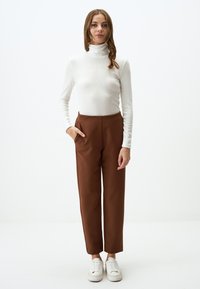 Maglione bianco a coste con colletto alto abbinato a pantaloni marroni a vita alta con tasche laterali, completato da sneaker bianche. Design semplice.
