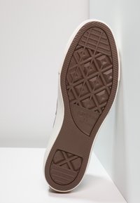 Sole bílé a šedé tenisky s hnědou texturovanou gumovou podrážkou se geometrickými vzory a logem "Converse All Star".