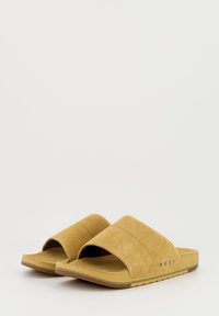 Sandales à glisser en suède beige avec une large sangle supérieure et une semelle intérieure texturée. Semelle en caoutchouc épaisse avec un détail de logo sur le côté.