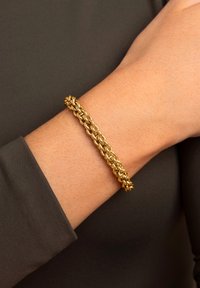 Złota metalowa bransoletka z plecionymi ogniwami i dekoracyjnymi akcentami, noszona na nadgarstku, z gładkim wykończeniem i błyszcząca powierzchnią.