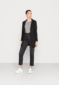Cappotto nero su misura indossato sopra un crop top a strisce zebrate bianche e nere, abbinato a jeans neri a vita alta e sneaker bianche con lacci.