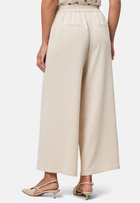Brede beige broeken met een elastische tailleband, een gestructureerde stof en twee achterzakken, gecombineerd met beige slingback hakken.
