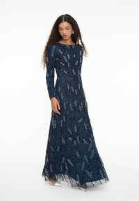 Navyblaue Langarmrobe mit silberner Floralstickerei und Pailletten, die eine taillierte Taille und einen fließenden Rock aufweist. Silberne Akzente an den Schuhen.