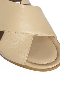 Beige Leder-Sandale mit einem breiten, überkreuzten Riemendesign, glatter Textur, offener Spitze und einer niedrigen, strapazierfähigen Sohle.