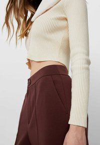 Crème rib gebreide cropped trui met een zachte kraag, gecombineerd met donkerbruin high-waisted broek met een knoop en zijzakken.