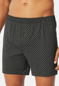 Shorts de bain noirs avec un motif géométrique blanc, taille élastique et un détail de bouton à l'avant pour un ajustement réglable.