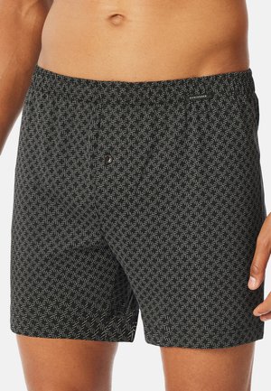 Zwarte zwembroek met een geometrisch wit patroon, elastische tailleband en een knoopdetail aan de voorkant voor een verstelbare pasvorm.