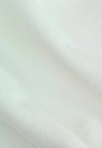 Tela de punto blanca con una textura suave, patrón de canalé fino y un ligero brillo, dispuesta en pliegues suaves para mostrar profundidad y superposición.