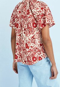 Korte mouwen shirt in een romige basis met rode bloemen- en paisleypatronen. Zachte, lichte stof; ontspannen pasvorm; gebogen zoom aan de achterkant.