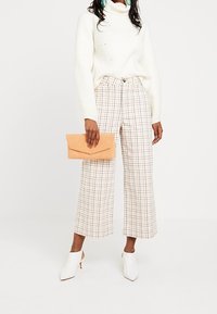 Vit stickad turtleneck-tröja, beiga rutiga vida byxor, vita klackiga mule-skor och en persiko-färgad clutch-väska. Texturerad, mönstrad, avslappnad outfit.