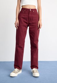 Jeans burgundii cu talie înaltă și picior drept, din denim, având buzunare frontale și închidere cu un singur buton. Purtați cu adidași cu model.