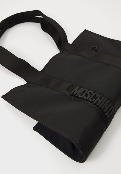 Black tote bag made of durable fabric, featuring a thick strap and a raised logo accent. The design is minimalistic with clean lines.