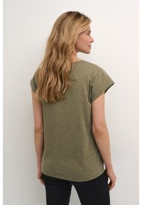 Oliivivihreä lyhythihainen t-paita rentoa leikkuuta, pyöreällä pääntiellä ja hieman kaarevalla helmallaan. Sileä pinta, ei näkyviä kuvioita tai koristuksia.