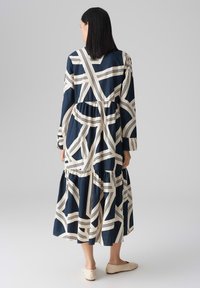 Navy and cream long-sleeve dress with abstract patterns, tiered design, relaxed fit, and ankle length. Fabric has a smooth texture.