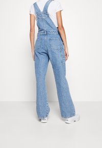 Helle blaue Denim-Latzhose mit lockerer Passform, verstellbaren Trägern und mehreren Taschen. Mit einer Vintage-Wäsche-Optik und weitem Bein-Design.