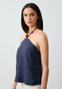 Top halter blu navy realizzato in materiale leggero, con una vestibilità comoda e una scollatura a barchetta, abbinato a una collana di perline multicolore.