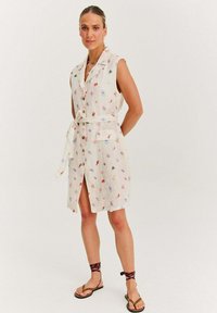 Sukienka lniana z kołnierzykiem, bez rękawów, w kolorowe kwiatowe wzory. Zawiera pasek w talii, guziki oraz kieszeń z przodu.