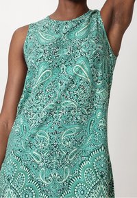 Robe sans manches en teal avec des motifs paisley et floraux complexes. Texture lisse, décolleté rond et design fluide.