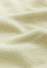 Tissu doux jaune pâle avec une texture subtile et des plis légers créant de légères ombres à la surface.