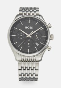 Montre chronographe avec bracelet en acier inoxydable, cadran noir, accents argentés, échelle tachymétrique et trois sous-cadrans pour les fonctions de chronométrage.