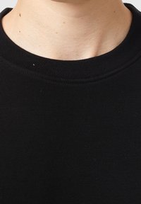 Camiseta negra de algodón con cuello redondo acanalado; textura lisa; costuras mínimas visibles alrededor del cuello.