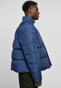 Navy blue puffer jacket with a high collar, featuring a quilted design and side zipper. Smooth texture and slightly oversized shape.