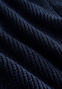 Tissu tricoté bleu foncé avec un motif texturé en forme de gaufre montrant des plis doux et des ombres.