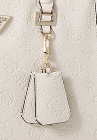 Bolso de mano de cuero blanco texturizado con patrones en relieve, cierre de hardware en tono dorado y una etiqueta desmontable con diseño a juego.
