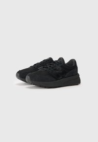Baskets de sport noires avec une combinaison de daim texturé et de matériaux en mesh, dotées d'une épaisse semelle noire et d'un design traditionnel à lacets.