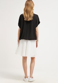 Sort, kortærmet bluse, parret med en hvid, tekstureret nederdel med et gittermønster. Hvide sneakers fuldender looket.