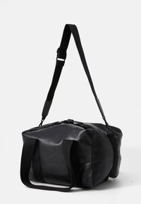 Black leather duffel bag with a smooth texture, featuring two fabric handles and a detachable adjustable strap for versatile carrying.