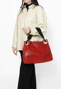 Borsa a tracolla intrecciata rossa con manici neri, dotata di elementi circolari in argento. La borsa ha una superficie textured e una forma morbida e sformata.