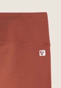 Leggings color ruggine realizzati in materiale elasticizzato, con una texture liscia e un piccolo logo bianco sulla vita.
