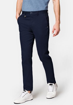 Granatowe spodnie o slim fit, wykonane z mieszanki bawełny. Posiadają szlufki na pasek, kieszenie z przodu i zamek błyskawiczny. Noszone z białymi trampkami.