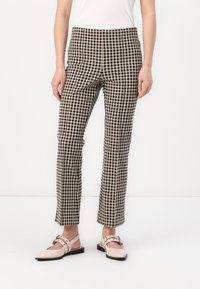 Pantalons à carreaux en tissu noir et beige, coupe ajustée, longueur cheville, avec une texture subtile. Associés à des chaussures plates beiges.