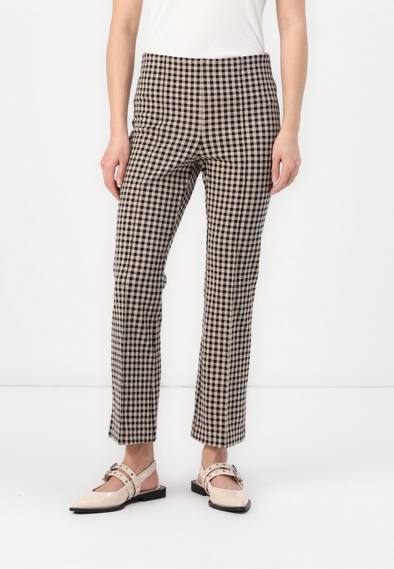 Pantalons à carreaux en tissu noir et beige, coupe ajustée, longueur cheville, avec une texture subtile. Associés à des chaussures plates beiges.