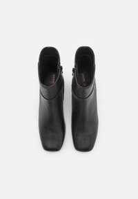 Paire de bottines en cuir noir avec bouts carrés et fermetures éclair latérales vues de dessus sur fond blanc.