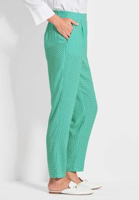 Grüne gemusterte Hosen verfügen über ein geometrisches Design mit abgerundeten Formen. Der Stoff hat eine leichtgewichtige Textur und enthält seitliche Taschen.