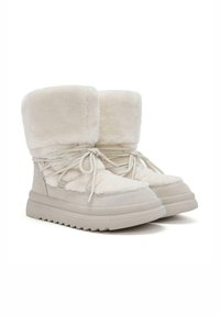 Botas de tobillo de imitación de piel de pelo blanco y ante con una suela gruesa, que presentan cordones, un borde doblado en la parte superior y acentos texturizados en los lados.