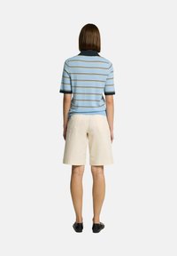 Blårandig polo med marinblå krage, tillsammans med beige shorts. Polon har korta ärmar och en åtsittande design. Svarta skor är på.